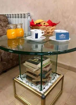 a glass table with books and a cup of coffee and a basket of fruit at Elena Hotel in Petrich
