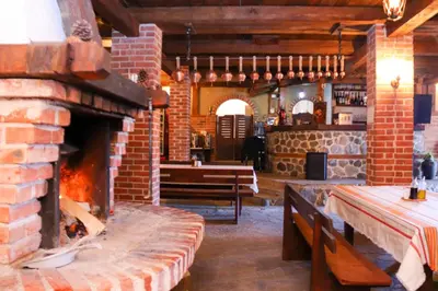 a restaurant with a brick fireplace and a table and bench at Семеен хотел Света Марина in Dobrinishte