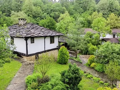 a small white house with a roof in a garden at Къща за гости КИМ in Apriltsi