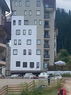 a woman walking in front of a tall building at STENATA Sport Apartments in Pamporovo