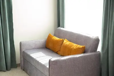 a yellow pillow sitting on a gray chair next to a window at Hotel Forum City in Pazardzhik