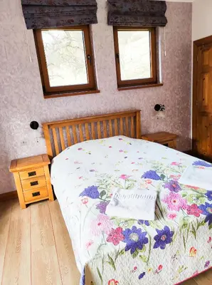 a bedroom with a bed with a floral bedspread and two windows at Терасите - Къща 2 in Ribarica