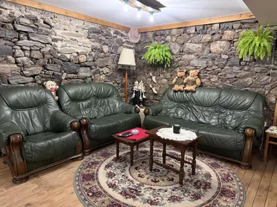 a living room with leather furniture and a stone wall at Къща за гости ЕМА in Vetren Dol