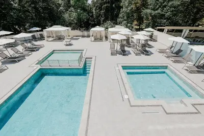 two swimming pools with lounge chairs and umbrellas in a pool at Hotel Green Park Service Perfected in Garmen