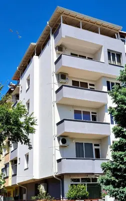 a tall white building with trees in front of it at Family Hotel Ambrozia in Sandanski