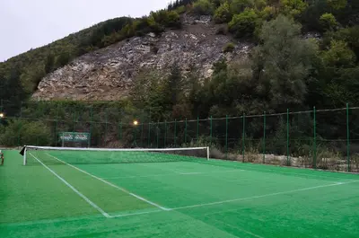 a tennis court with a mountain in the background at Fisherman's Hut Family Hotel in Beden