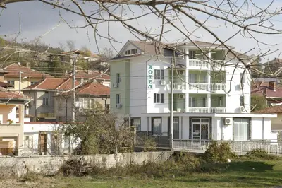 a white building with a green sign on it at Karadzhovy Guest House in Kalofer