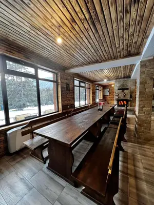 a large wooden table in a room with windows at Райски кът “Еленова поляна” in Dobărsko