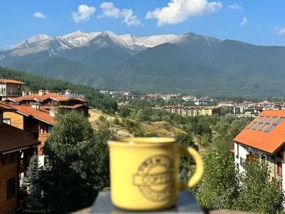 a yellow coffee cup sitting on a ledge with mountains at Cozy duplex apartment in St. John Park in Bansko