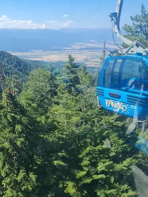 a blue cable car flying over trees on a mountain at Aspen Golf D 401 in Bansko