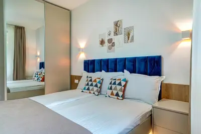 a bedroom with a bed with a blue headboard and a mirror at N.Joy Holiday Apartment 532 by Oak Residence in Smolyan