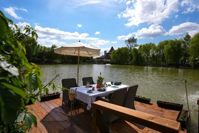 a table with an umbrella on a deck next to a lake at Glass Domes - by The Wind Mills Hydropark in Gorna Malina