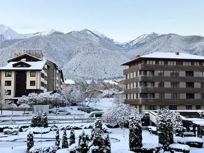 a building covered in snow with mountains in the background at PANORAMA SPA ASPEN APARTMENT in Razlog