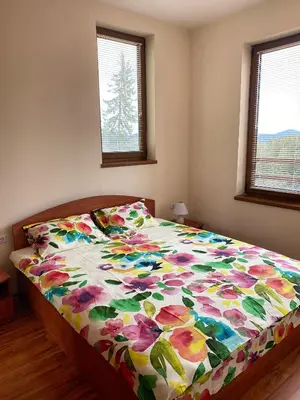 a bed with a floral comforter in a bedroom at Cedar Heights Cozy Apartments in Pamporovo