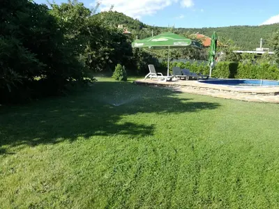 a yard with a green umbrella and a swimming pool at Къща за гости Вила Смокиня град Хисаря in Hisarya