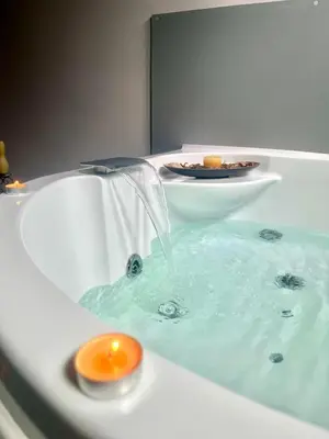 a bath tub filled with blue water with a candle at Хотел Дикас in Smolyan