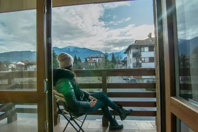 a man sitting in a chair on a balcony looking out a window at Banderitsa Apartment 2 in Bansko