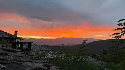 a sunset in the mountains with a house in the foreground at Кътче in Leshten