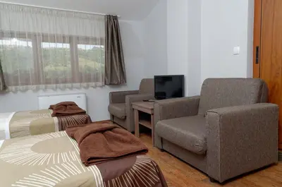 a bedroom with two beds and a chair and a television at Alpine Garden Hotel (Trayanovi Dvori) in Simitli