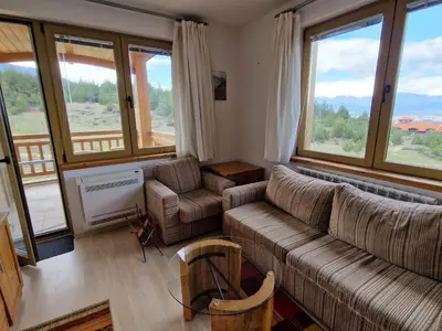 a living room with a couch and chairs and windows at Saint John Hill Apartment in Bansko