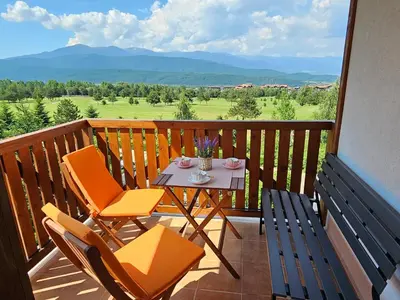 a table and chairs on a balcony with a view at Green Peaks Suite in Pirin Golf & County Club in Razlog