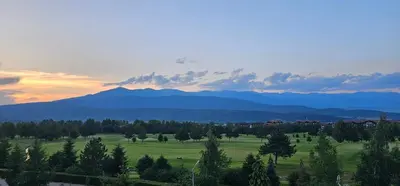 a field with trees and mountains in the distance at Green Peaks Suite in Pirin Golf & County Club in Razlog