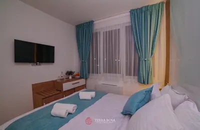 a bedroom with a bed with blue curtains and a television at Хотел Терра Роза in Karlovo