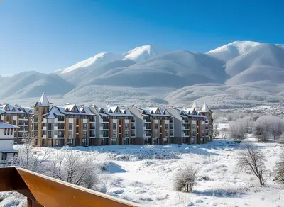 a building in the snow with mountains in the background at Belvedere Holiday Club К505 Sunset View in Bansko