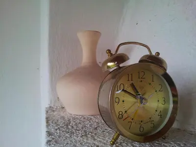 an alarm clock sitting next to a pink vase at СПА къща за гости Каза Роза - Swiss Style Chalet Casa Rosa SPA Guest House in Kyustendil