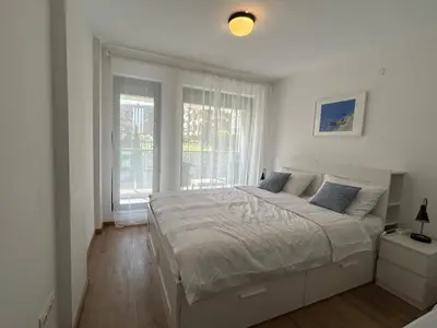 a white bedroom with a large bed and a window at Idea Apartment in Sofia