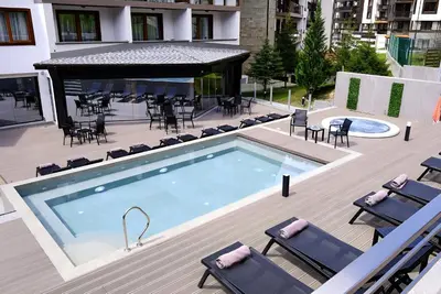 a swimming pool on a deck with chairs and a building at Cozy apartment in luxury SPA resort St Ivan Rilski Bansko -free wellness & parking- in Bansko