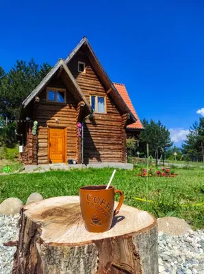 a coffee cup sitting on a tree stump in front of a log cabin at Lambievi Kolibi in Gorno Kraishte