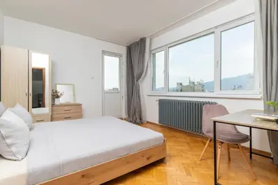 a bedroom with a bed and a desk and windows at Black Peak Panorama central apartment in Sofia