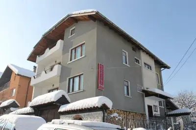 a building covered in snow with cars parked in front at Дамянова Къща in Dobrinishte