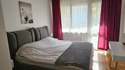 a bedroom with a bed and a window with red curtains at Business Park Retreat: 1BR with Mountain View in Sofia