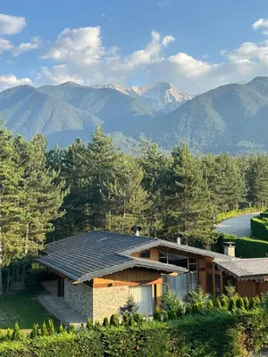 a house with a solar roof with mountains in the background at Pirin Golf Mountain View Apartment in Razlog