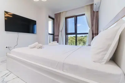 a white bedroom with a large bed with a flat screen tv at Lauta Forest 1-bedroom apartment in Plovdiv