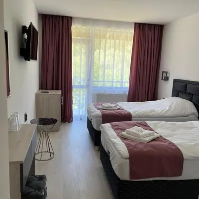 a hotel room with two beds and a television at Хотел Лилия in Rudozem