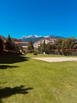 a field of grass with buildings and mountains in the background at View Apartment Bansko Royal Towers in Bansko