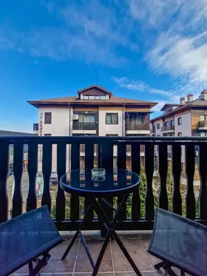 a table on a balcony with two chairs and a house at Cosy Apartment On The Lift in Bansko