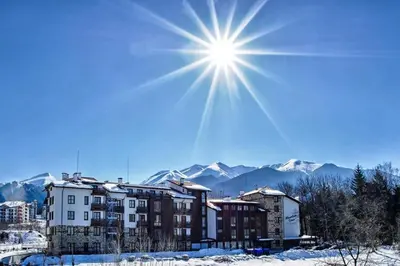 a building in the snow with the sun in the sky at Mountain Studio - Ski in and out - FREE Spa in Bansko