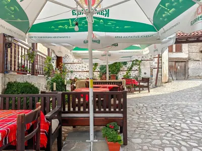 a patio with tables and a green and white umbrella at Todeva House Hotel and Tavern in Bansko
