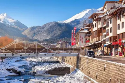a bridge over a river in a town with snowy mountains at Alpin Penthouse 2 Bedroom with Fireplace and Mountain View in Bansko