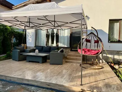 a patio with a white umbrella and a swing at Вила Динати in Perushtitsa