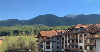 an apartment building with mountains in the background at Mountain View Apartment with Balcony & Ski Access nearby - Serendipity in Bansko