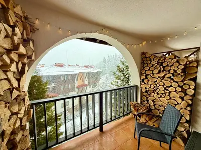 a balcony with a large window with a pile of logs at GS SKI Apartment - The Grand Monastery Pamporovo in Pamporovo