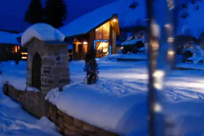 a snow covered yard with a stone wall in front of a house at Ski liviomoritz at gma il com Chalet in Madzhare