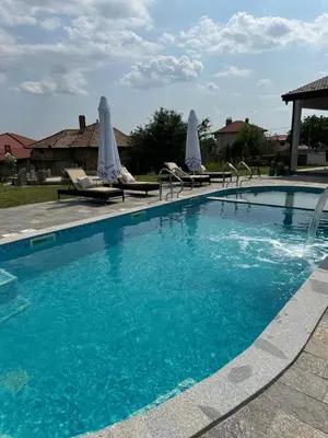a large blue swimming pool with chairs and umbrellas at Къща за гости Casa La Tinozza in Hisarya