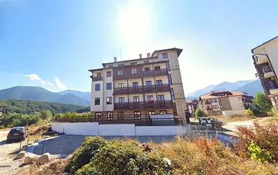 a building on a hill with mountains in the background at Pirin Heights Apartment 200m from SKI ROAD in Bansko