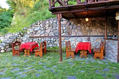 two tables and chairs with red table cloths in front of a stone wall at Melnik Pyramids Guesthouse in Zlatkov Chiflik
